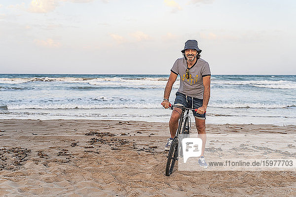 Älterer Mann sitzt auf seinem Fahrrad am Strand