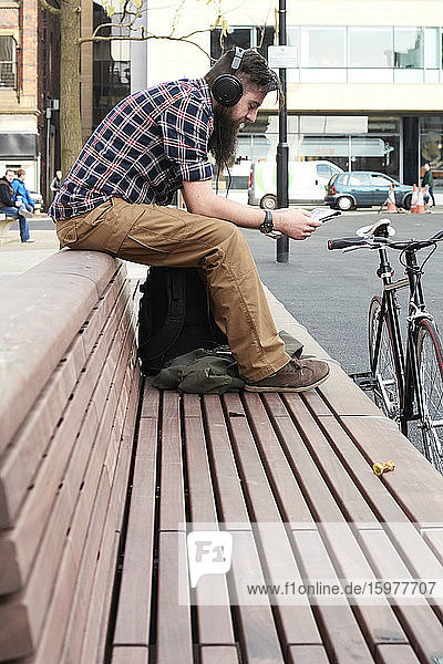 Side view of bearded mid adult man reading newspaper while sitting on bench in city