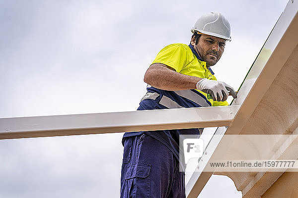 Mature technician measuring roof while standing against sky