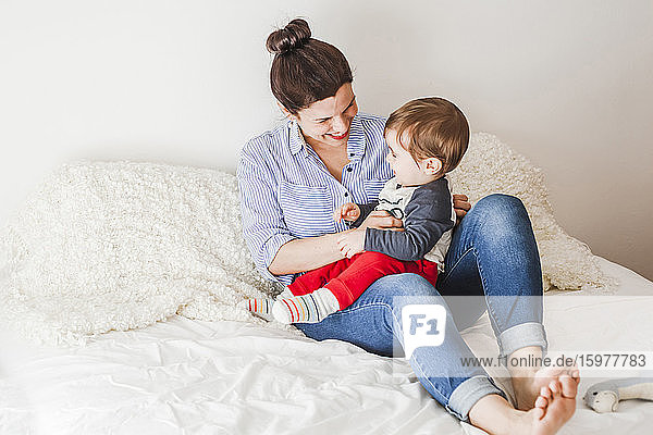 Glückliche Mutter sitzt auf dem Bett und spielt mit ihrem kleinen Sohn