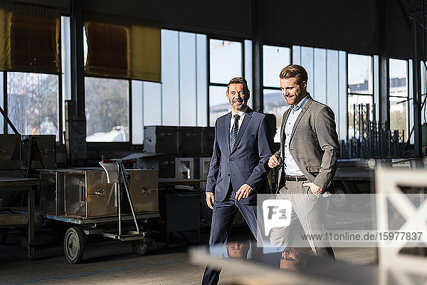 Zwei lächelnde Geschäftsleute gehen in einer Fabrik