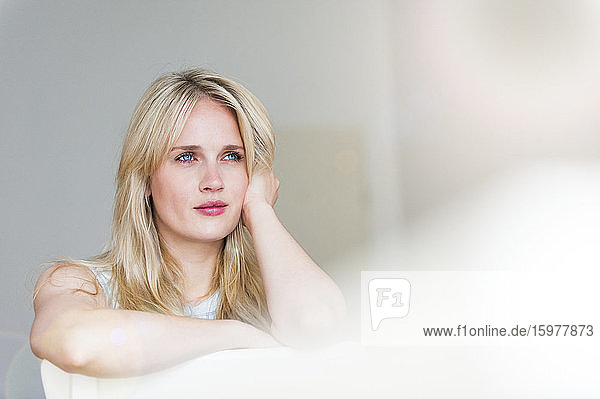 Porträt einer nachdenklichen blonden Frau mit blauen Augen  die sich an eine Rückenlehne lehnt
