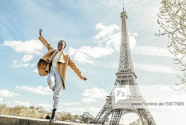 Excited woman jumping from retaining wall with Eiffel Tower in background Paris France