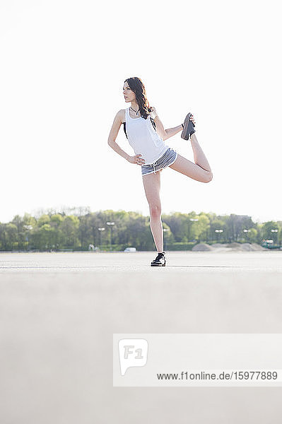 Young woman exercising on land against clear sky during sunny day