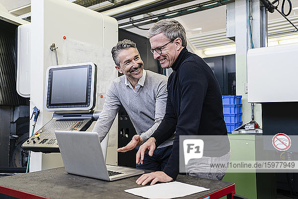 Happy male supervisors discussing over laptop in factory