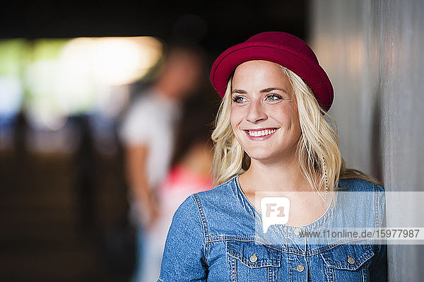 Portrait of happy young woman wearing red hat leaning against wall