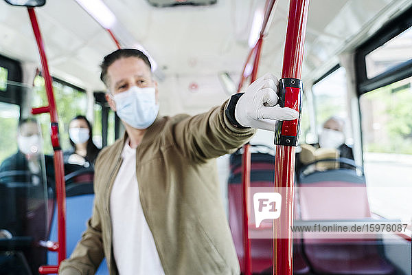 Mann mit Schutzmaske und Handschuhen in einem öffentlichen Bus  der die Stopptaste drückt  Spanien