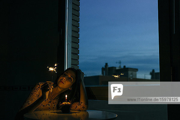 Geburtstag Frau hält Wunderkerze  während mit Cupcake zu Hause bei Sonnenuntergang sitzen