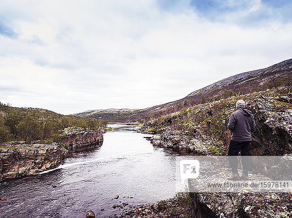 Norwegen  Troms og Finnmark  Lakselv  Männlicher Wanderer bewundert Aussicht auf Fluss und umliegende Landschaft