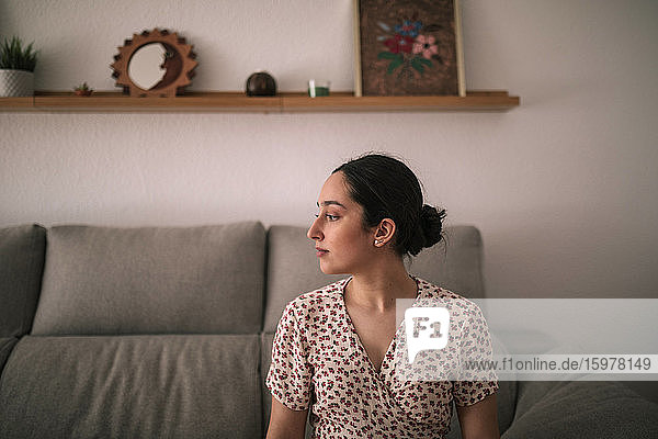 Nachdenkliche junge Frau sitzt zu Hause auf dem Sofa