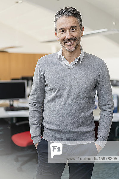 Portrait of smiling handsome businessman standing with hands in pockets at office