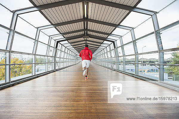 Rückansicht eines jungen Mannes  der auf einem Skywalk läuft
