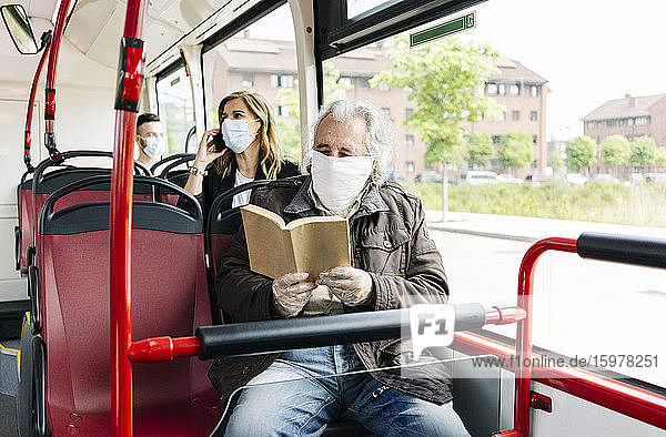 Älterer Mann mit Schutzmaske im öffentlichen Bus beim Lesen eines Buches  Spanien
