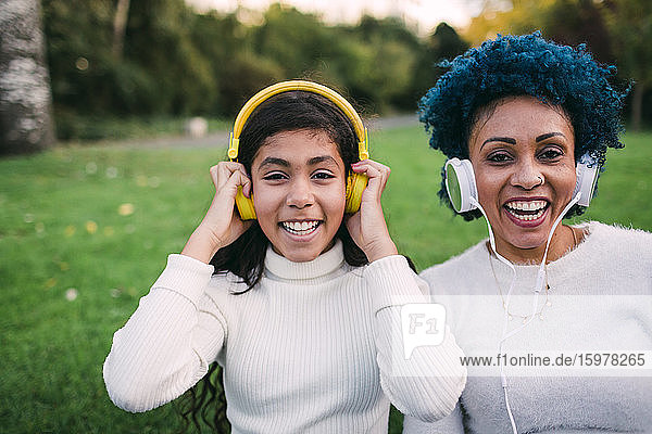 Glückliche Mutter und Tochter hören Musik über Kopfhörer im Park