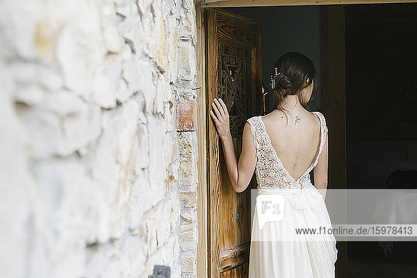 Rear view of woman in elegant wedding dress at door