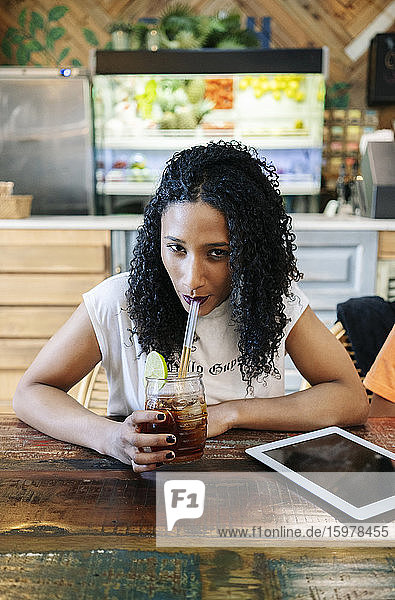 Porträt einer selbstbewussten jungen Frau  die in einem Restaurant Eistee trinkt