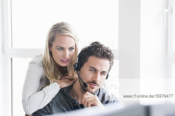 Geschäftsfrau lehnt sich an einen männlichen Kundenbetreuer  der ein Headset trägt  während sie einen Computer im Büro benutzt