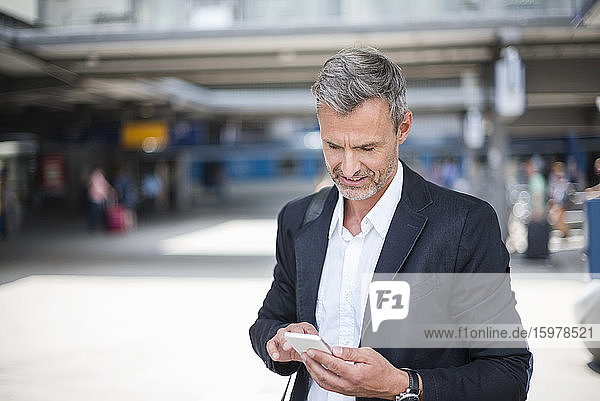 Geschäftsmann  der ein Smartphone benutzt  während er am Bahnhof steht