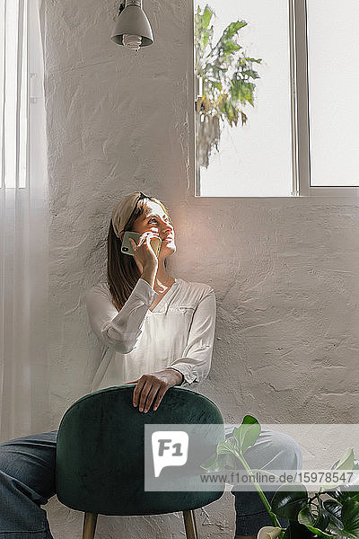 Schöne Frau  die ihr Smartphone benutzt  während sie auf einem Stuhl an der Wand zu Hause sitzt