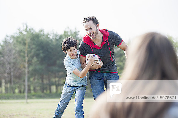 Fröhlicher Vater und Sohn spielen Rugby mit Frau im Vordergrund im Park
