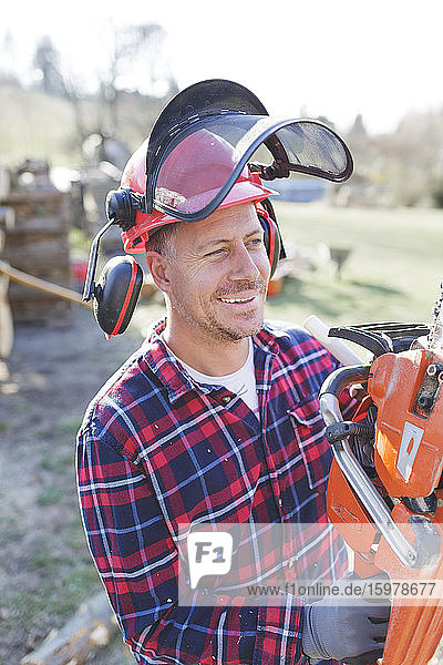 Thoughtful lumberjack holding chainsaw during sunny day