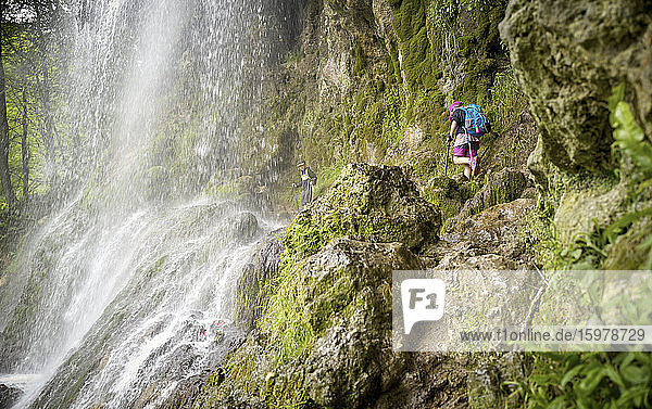 Geschwister wandern auf einer Felsformation unter dem Uracher Wasserfall im Wald