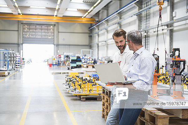 Zwei Männer benutzen einen Laptop in einer Fabrikhalle