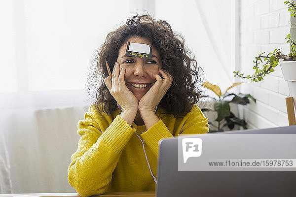 Portrait of woman sitting at desk in home office with adhesive note on her forehead