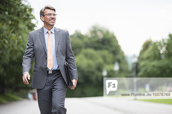 Smiling businessman looking away while walking on road against sky