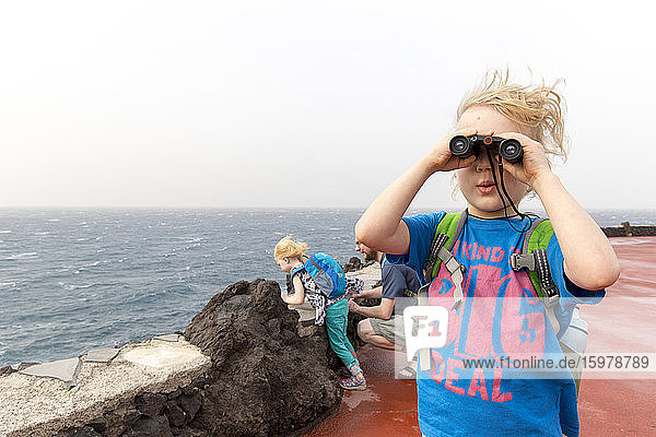 Neugieriger Junge  der durch ein Fernglas schaut  während er mit seiner Familie an der Costa Adeje  Kanarische Inseln  Spanien  Urlaub macht