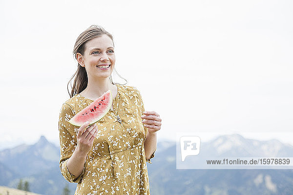 Beautiful smiling woman holding watermelon slice while standing against sky