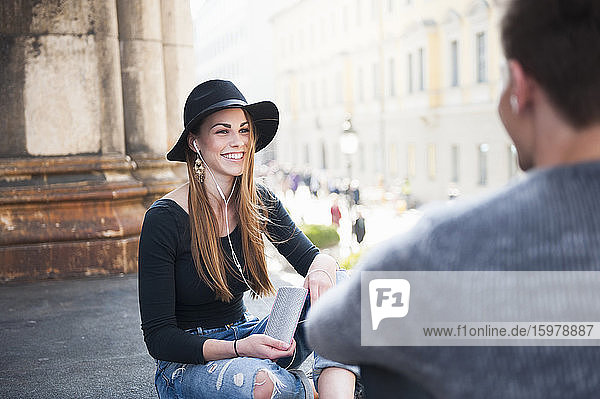 Happy young woman looking at man while listening music in city
