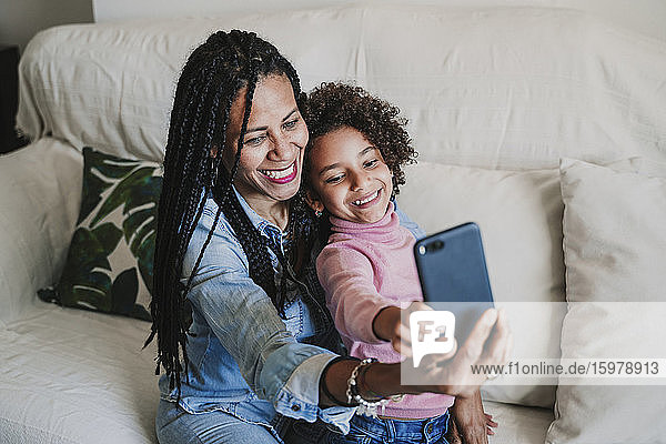Porträt einer glücklichen Mutter und ihrer kleinen Tochter  die ein Selfie mit ihrem Smartphone auf der Couch machen
