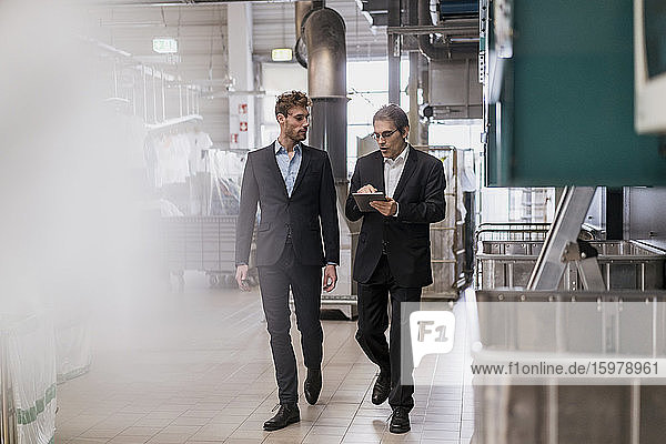 Two businessmen with tablet walking in a factory
