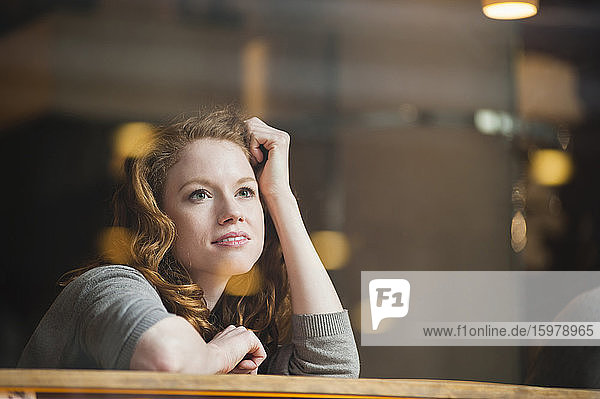 Nachdenkliche Frau  die sich auf einen Tisch stützt  gesehen durch ein Glasfenster in einem Café