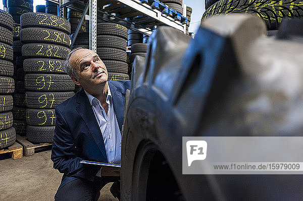 Confident senior businessman looking up while crouching by tire at store