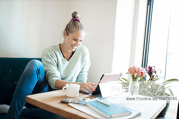 Lächelnde junge Frau  die im Büro zu Hause ein digitales Tablet benutzt