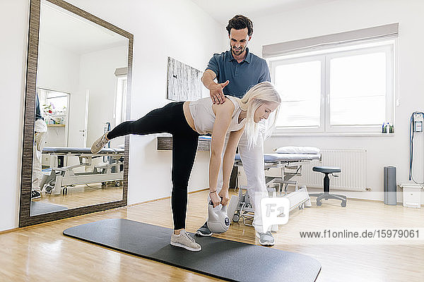 Physiotherapist assisting female patient  balancing on gym mat