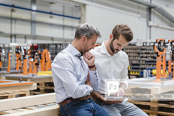 Two men sharing tablet on factory shop floor