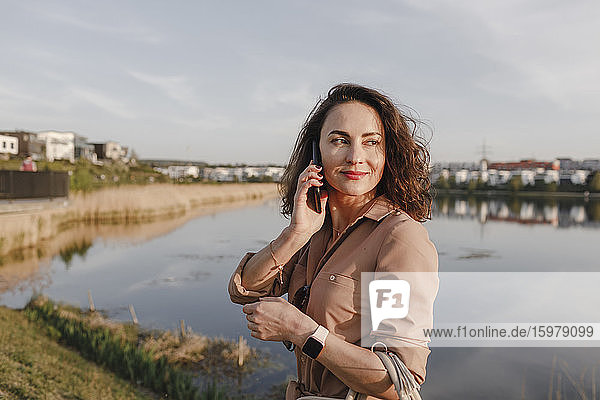 Schöne Geschäftsfrau schaut weg  während sie ihr Smartphone am Seeufer benutzt