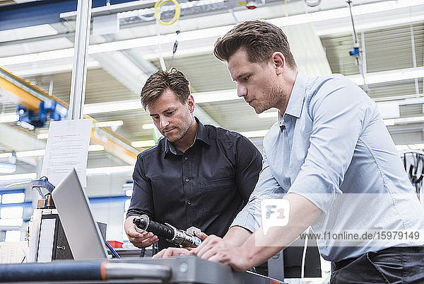 Two men using laptop in factory