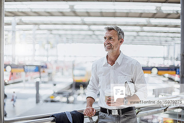 Nachdenklicher Geschäftsmann mit Kaffee in der Hand  der wegschaut  während er am Geländer steht