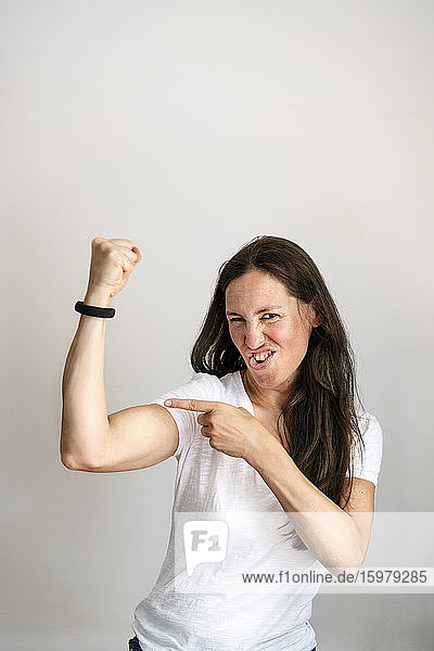 Portrait of cheerful mature woman pointing at bicep against white background
