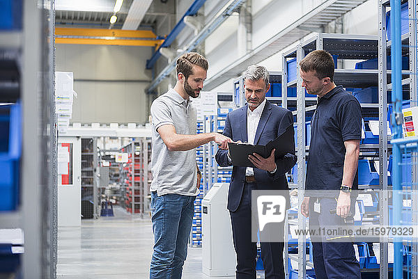 Three men talking in storehouse of a factory