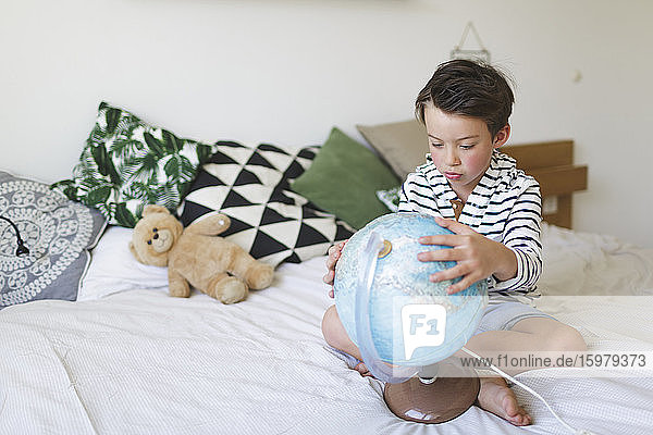 Porträt eines kleinen Jungen auf dem Bett sitzend mit seinem Globus