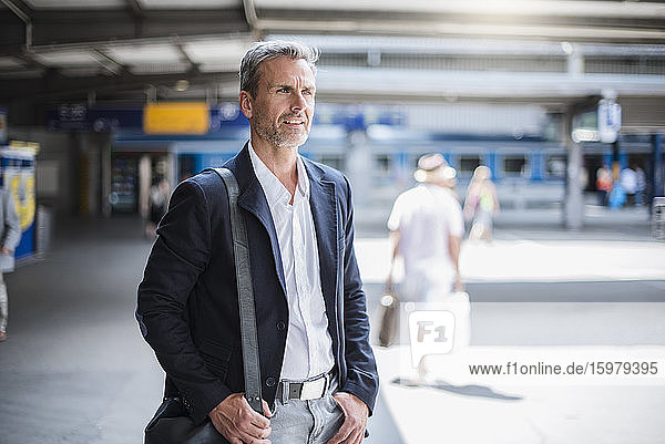 Smiling businessman looking away while standing at railroad station