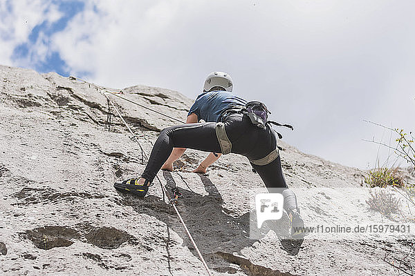 Young woman moving up while climbing rock against sky