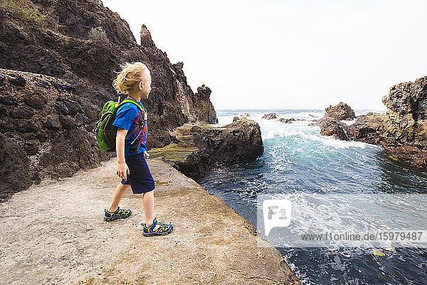 Full length of boy standing on rock formation while exploring sea at Costa Adeje  Canary Islands  Spain