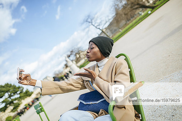 Junge Frau knutscht  während sie ein Selfie mit ihrem Smartphone am Straßenrand in Paris  Frankreich  macht