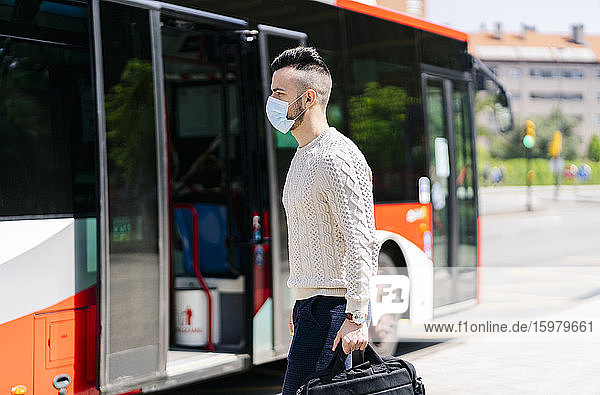 Junger Mann mit Schutzmaske vor einem Linienbus  Spanien